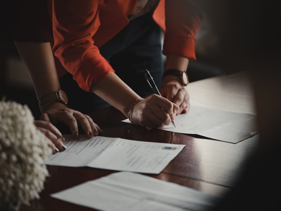 Firma de documentos legales sobre mesa de madera. Persona con camisa naranja y reloj.