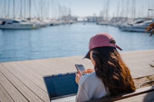 Emprendedora usando laptop y móvil en un puerto para crear su empresa online barata con MiempresaYA