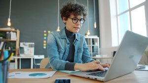 Profesional con gafas crea su empresa mientras trabaja, asesorada por MiempresaYA desde su oficina moderna