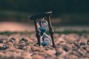 Reloj de arena con arena azul sobre piedras, símbolo del tiempo que tarda constituir una SL con MiempresaYA en Madrid